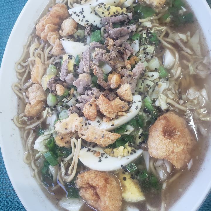 A big bowl of batchoy noodle soup topped with boiled eggs, crushed chicharon and green onions