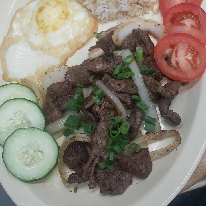 Tapsilog plate with marinated beef and onions, garlic rice, a fried egg, tomato and cucumber slices
