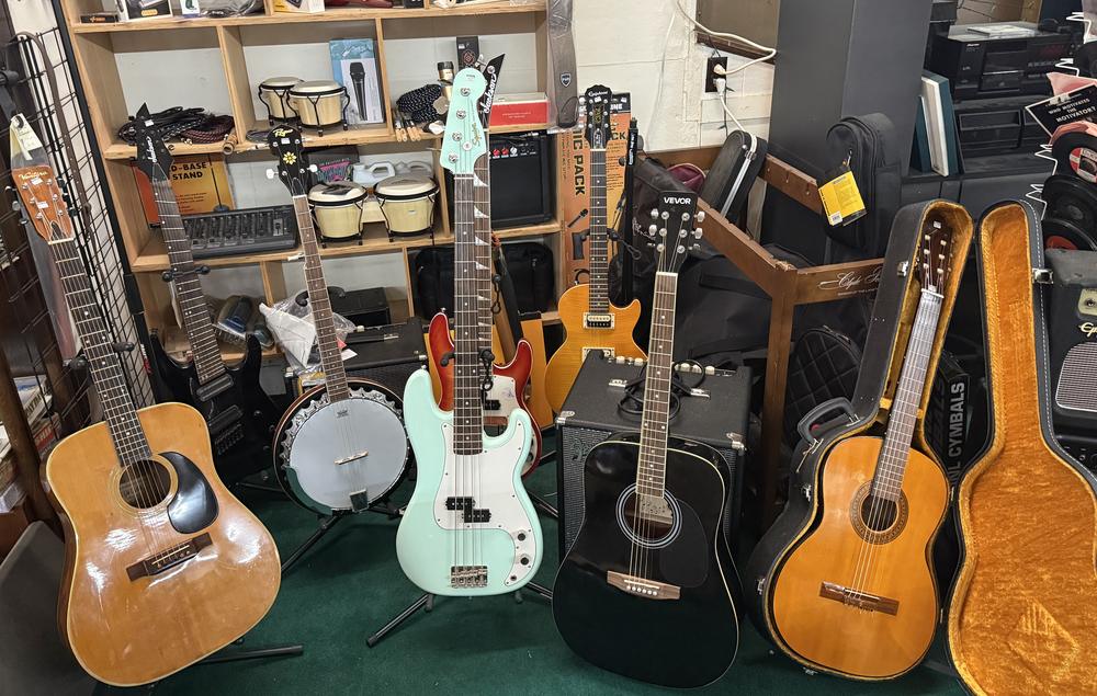 Acoustic guitars, a banjo, a mint green bass guitar and amps in the music corner