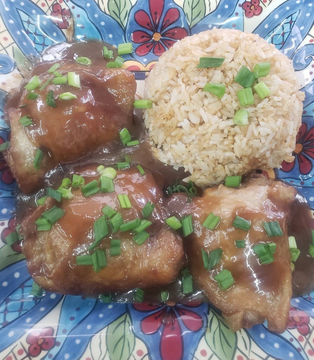 Glazed chicken adobo thighs topped with green onions next to a scoop of garlic rice on a hand painted plate