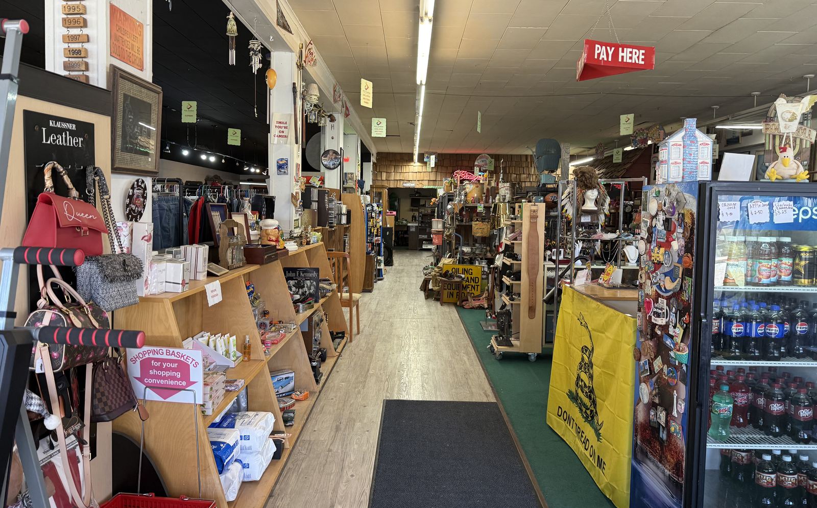 The main aisle of DTF Trading with shelves of goods, shopping baskets and a Pay Here sign overhead