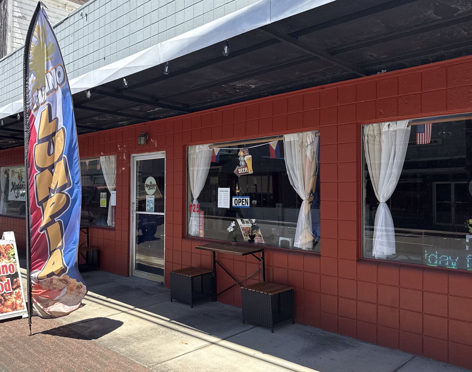 Red brick storefront of Mindanao's Best with a Filipino Food sidewalk sign and a lumpia flag