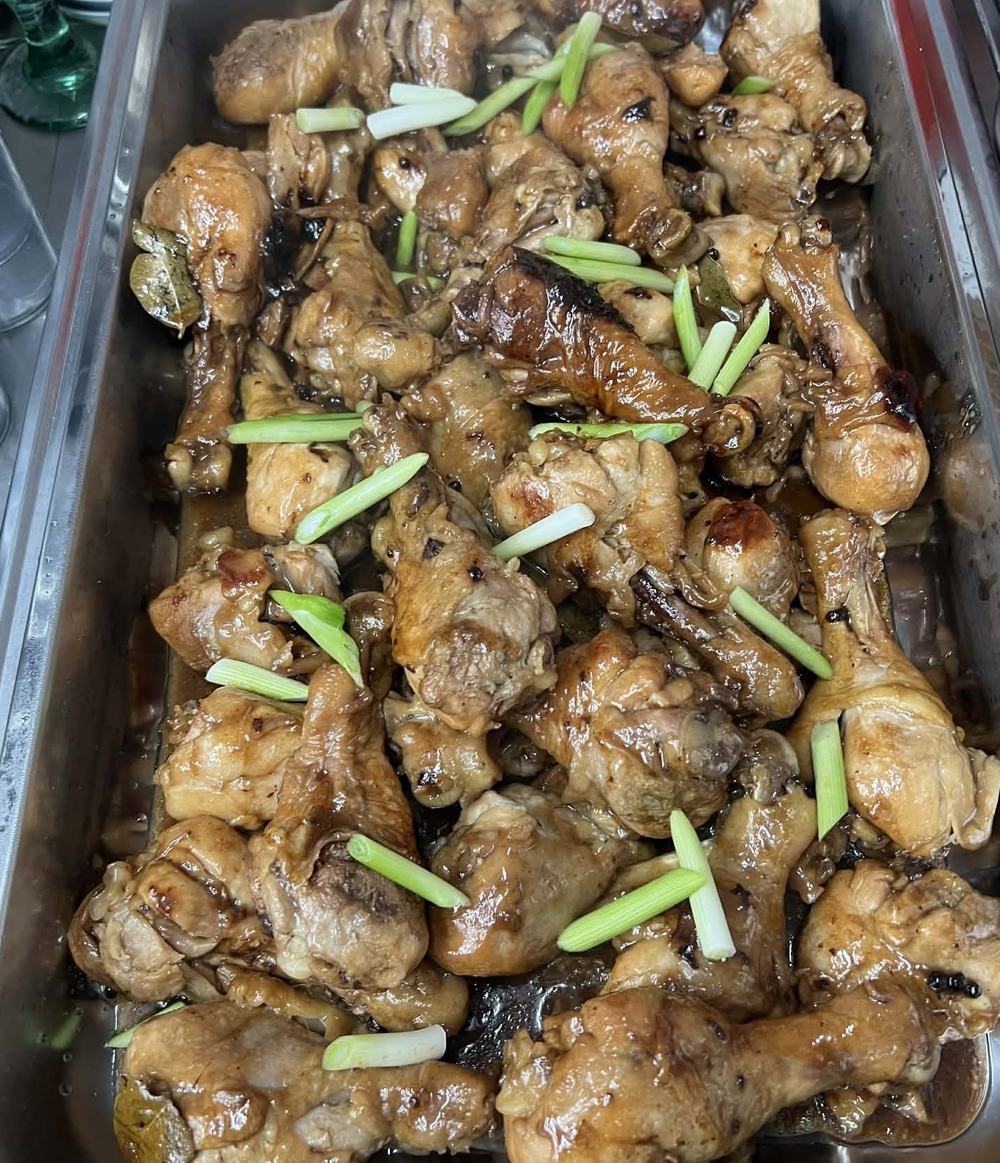 A full catering pan of chicken adobo drumsticks with bay leaves and green onions